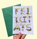 Greeting card with gilda design spelling "Felicitats" with green envelope held by a hand on a light yellow background